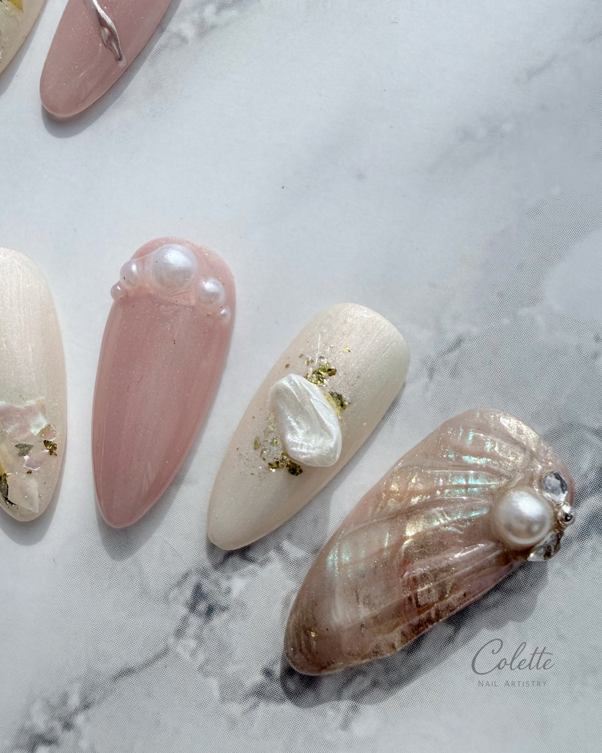 Close-up of Pearl Mist press-on nails featuring a shell-inspired design, pearls, gold foil and soft pink and ivory tones.