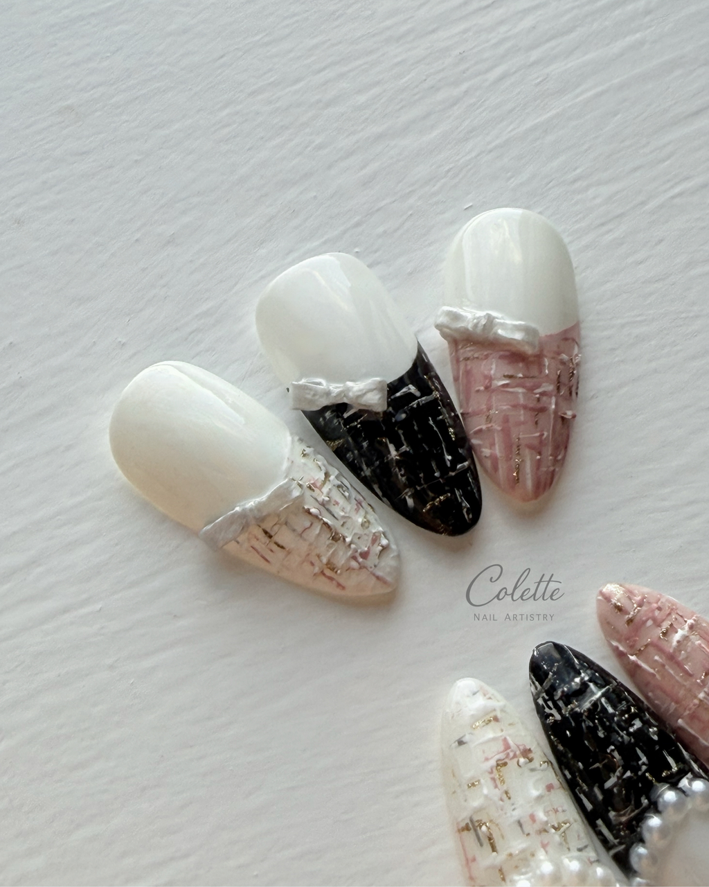 Close-up of Tweed Glow press-on nails, featuring black, pink and white tweed textures with pearl, 3D bow and metallic gold details.